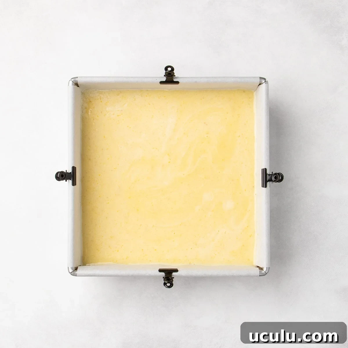Square pan filled with a smooth pale yellow layer over the crust, spread evenly to the edges.