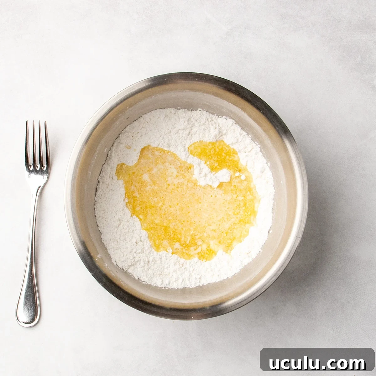 Melted butter mixture poured over white dry ingredients in a metal mixing bowl.