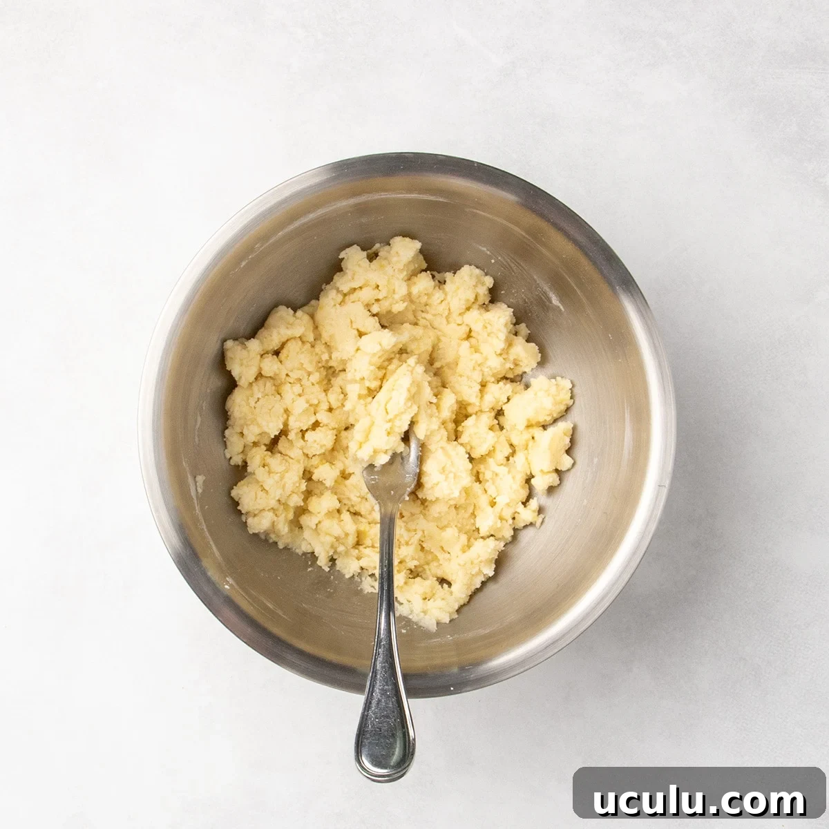 Clumpy pale dough mixture in a metal bowl with a fork.
