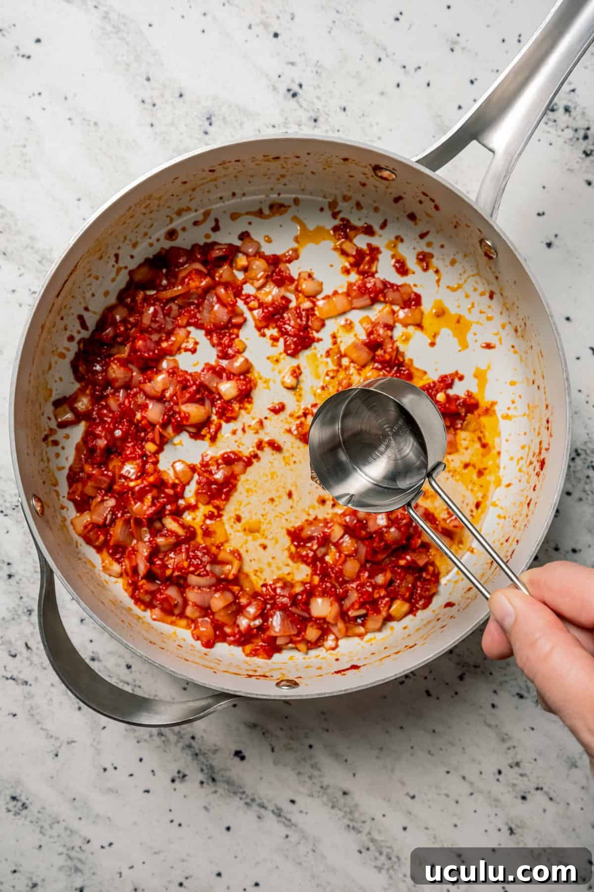 A spoonful of pasta water is added to onions sauteed in tomato paste in a skillet.