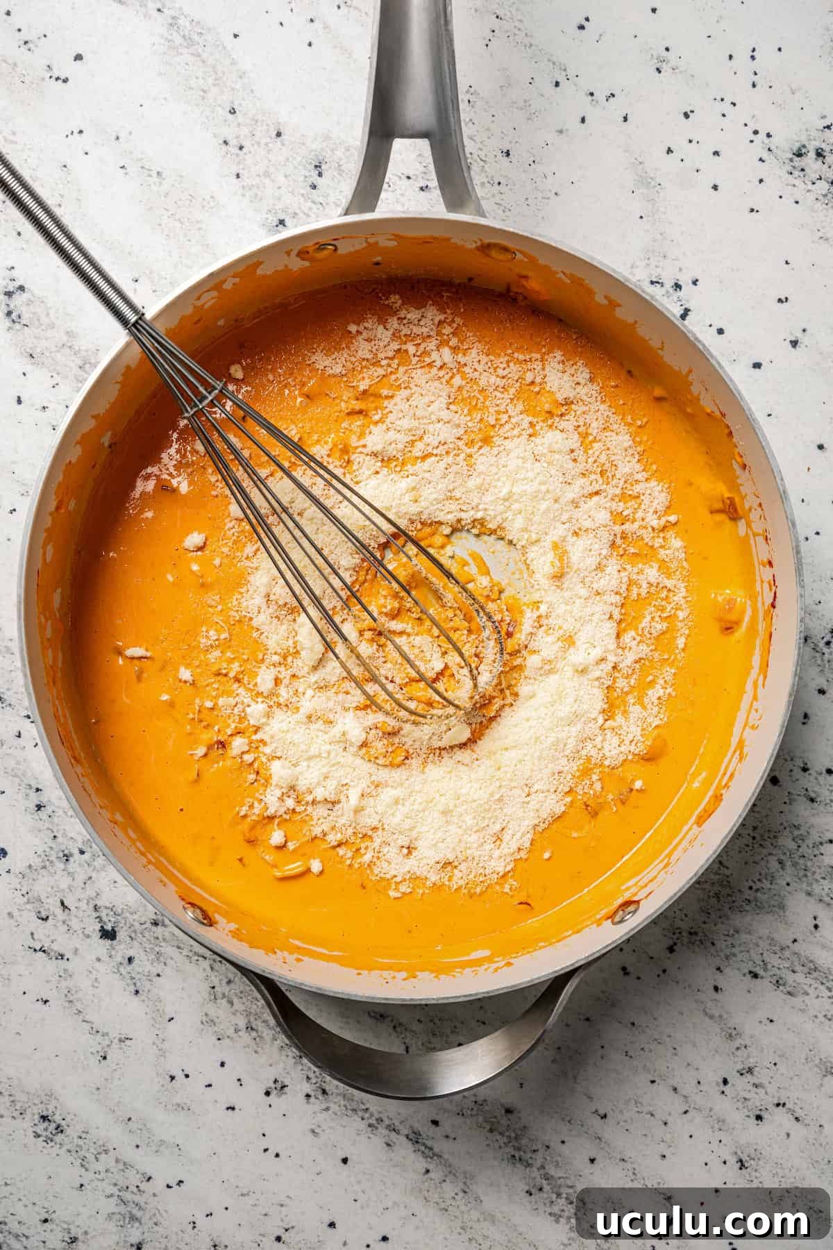 Grated parmesan cheese partially whisked into a skillet of vodka sauce.