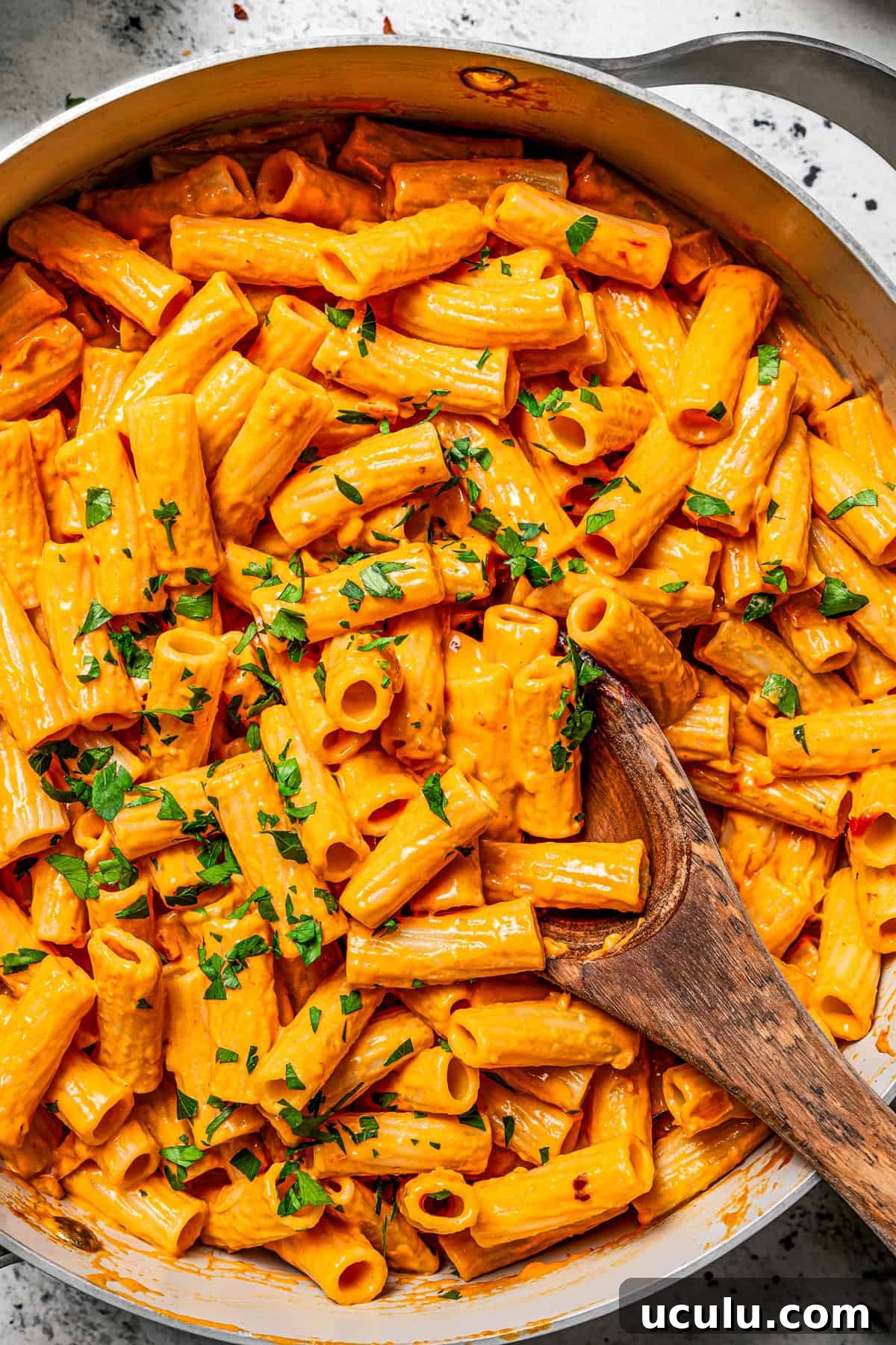 Photo of cooked tube pasta in a skillet with a wooden spoon stirring through it.