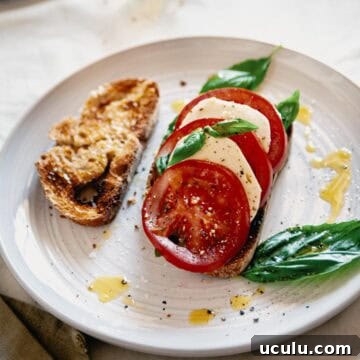 caprese bruschetta served on a plate with an extra slice of toasted bread.