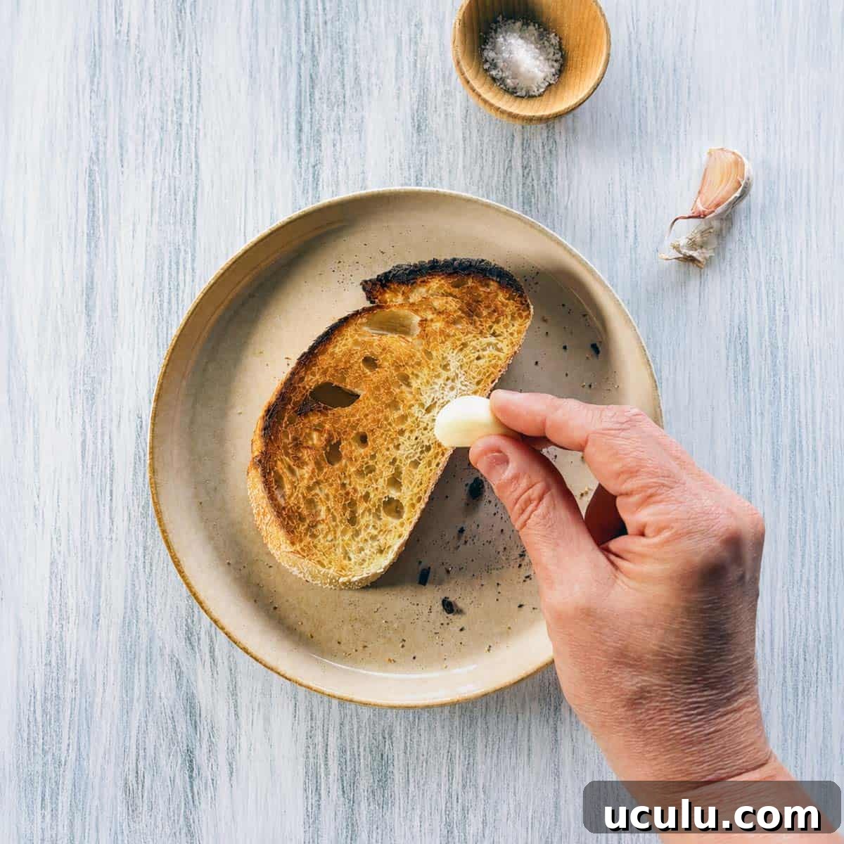 toasted sourdough being rubbed with a garlic bulb.