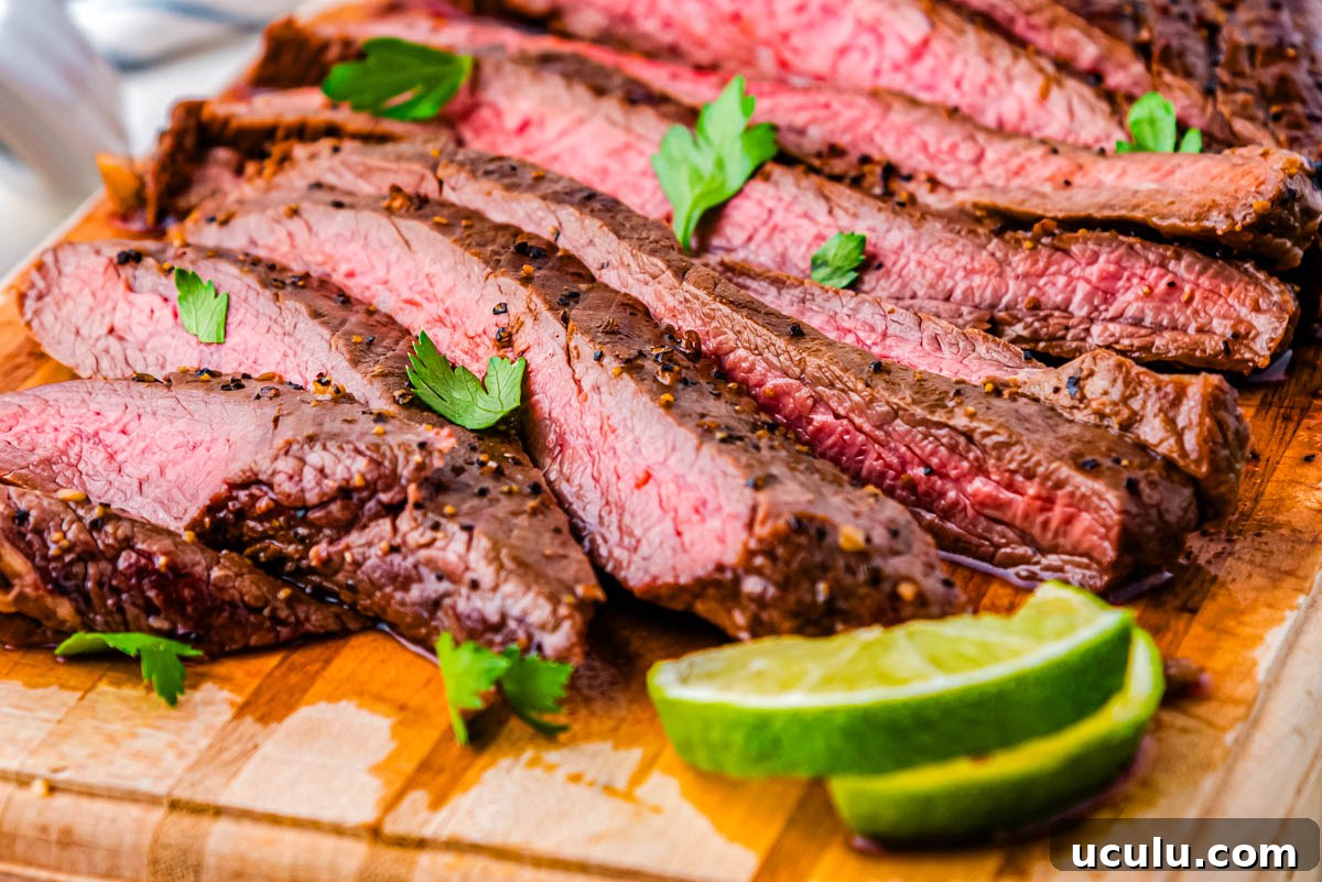 Slices of cast iron flank steak on a wooden cutting board garnished with parsley and fresh lime wedges.
