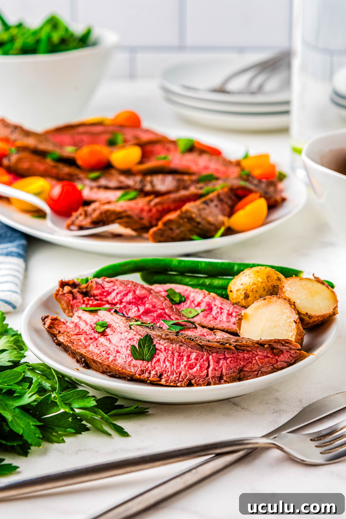 Slices of flank steak on a white plate with potatoes and green beans.
