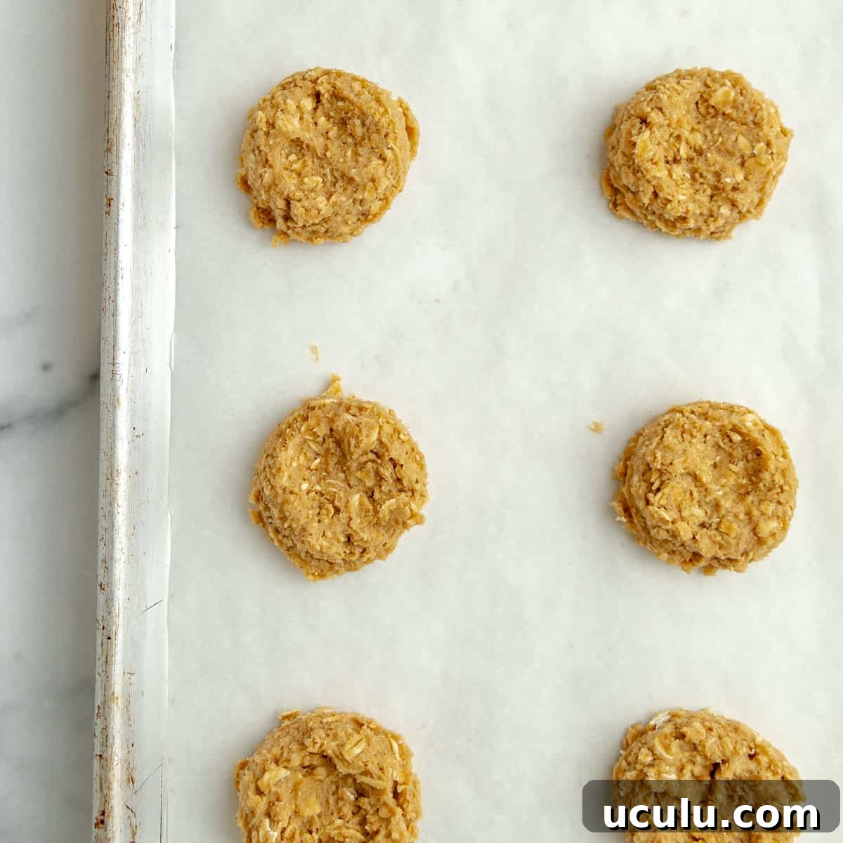 An up close image of cookie dough on a pan, the middles flattened slightly.