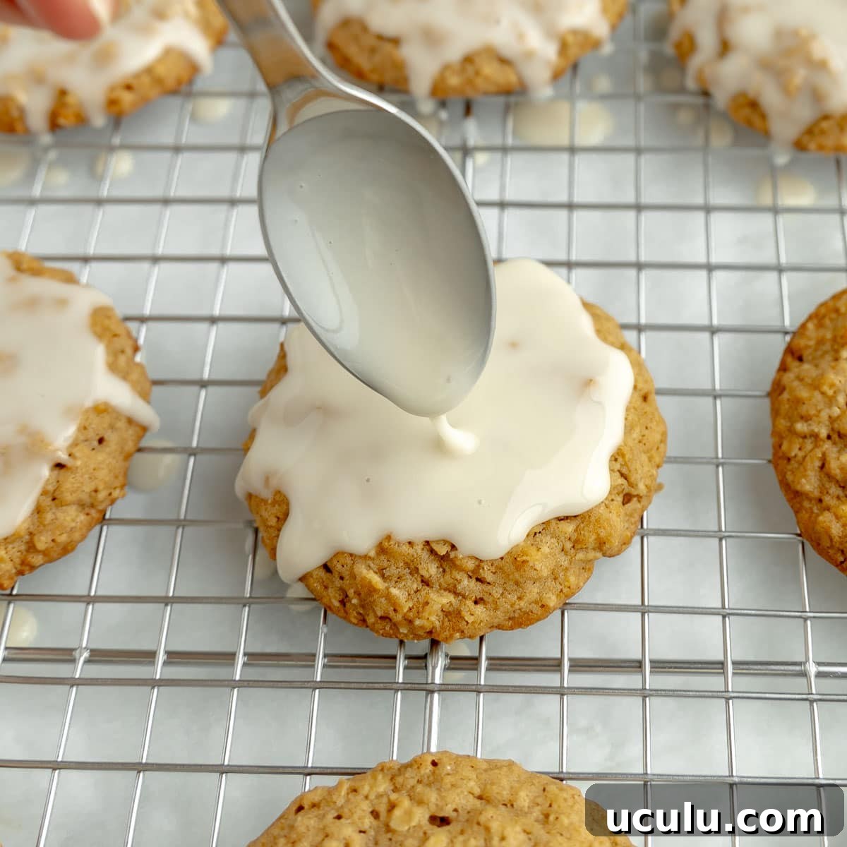 A spoon drizzling icing over oatmeal cookies.