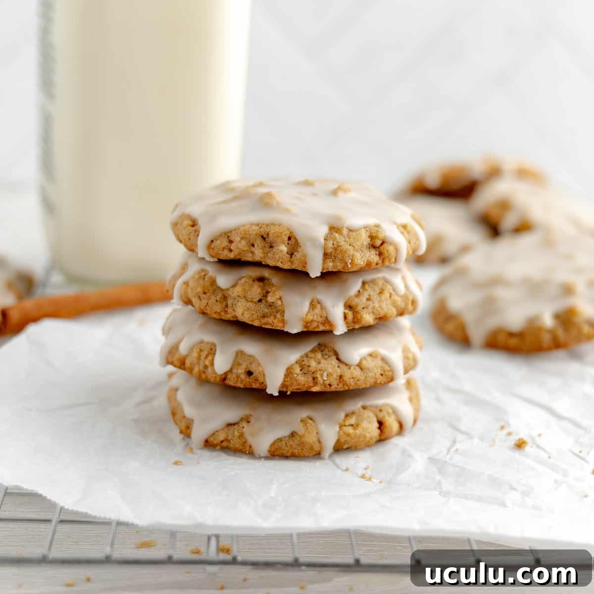 A stack of iced oatmeal cookies on white paper. Milk, cookies and cinnamon in the background.