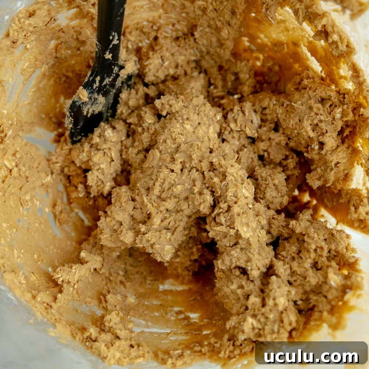 Iced oatmeal cookie dough in a bowl with a black spatula.