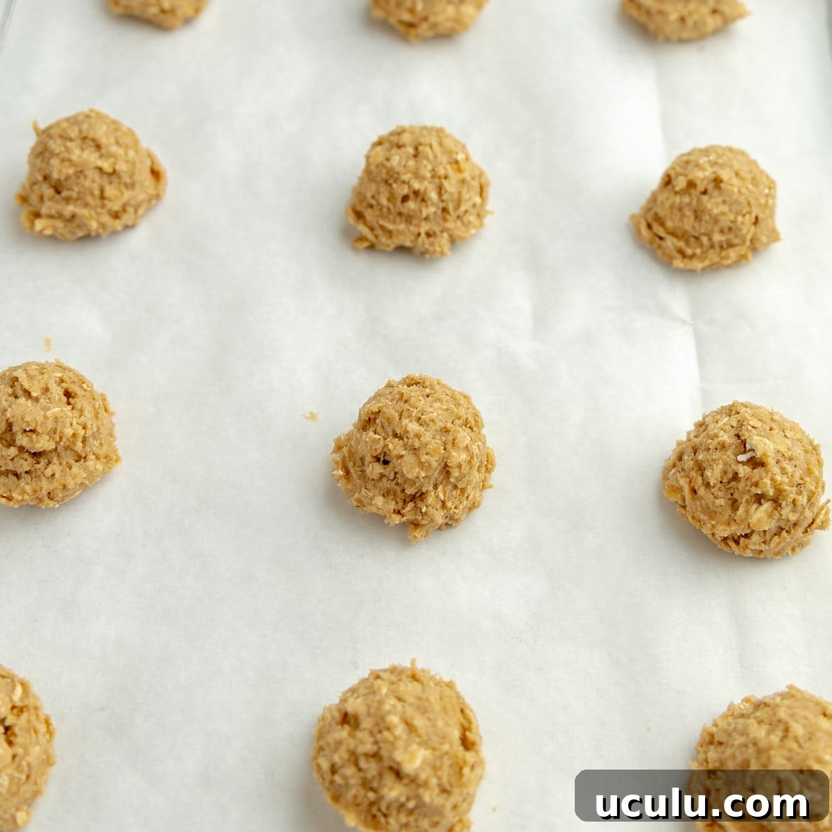 Balls of cookie dough on a parchment paper lined sheet pan.