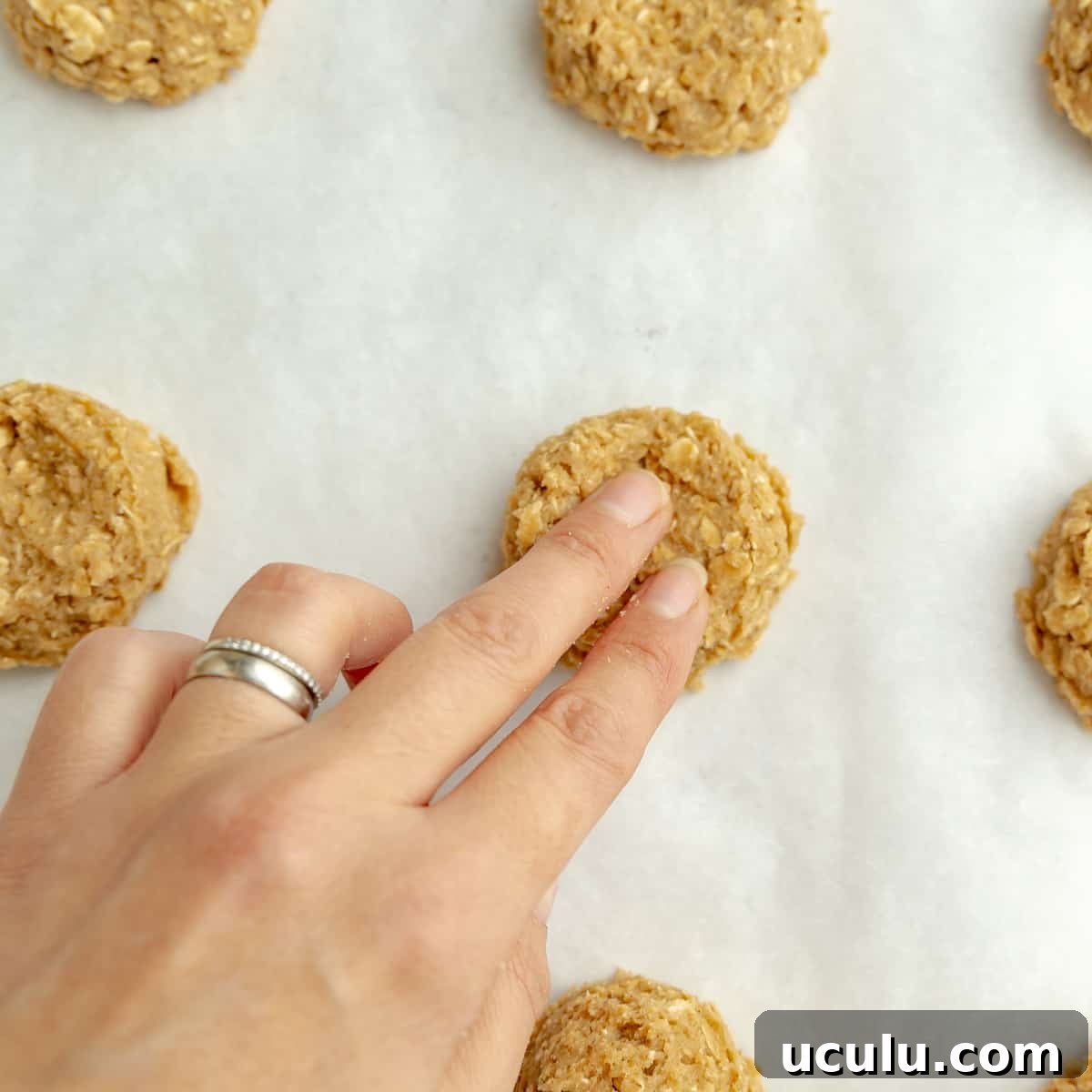 Two fingers flattening the center of the oatmeal cookies.