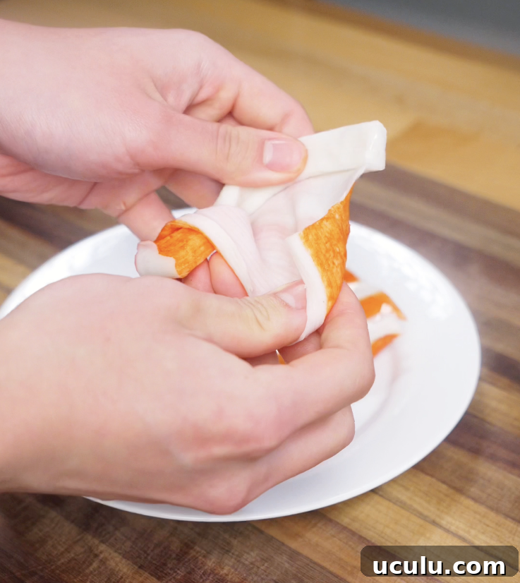 Hands pull apart imitation crab sticks into thin, shredded pieces for the creamy sushi bake topping.