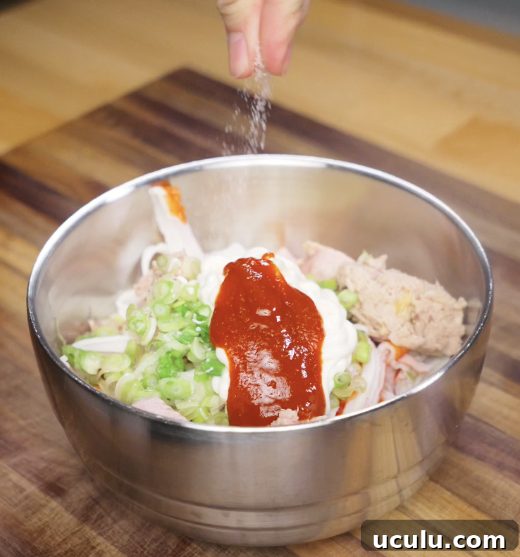 A bowl filled with crab, tuna, scallions, mayo, sriracha, and seasoning is being mixed to make the sushi bake topping.