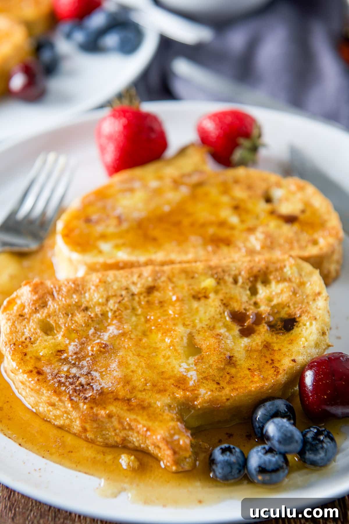 Close up of two pieces of French toast smothered with maple syrup on a plate with fruit