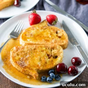 French toast smothered with maple syrup on a white plate with cherries, strawberries and blueberries