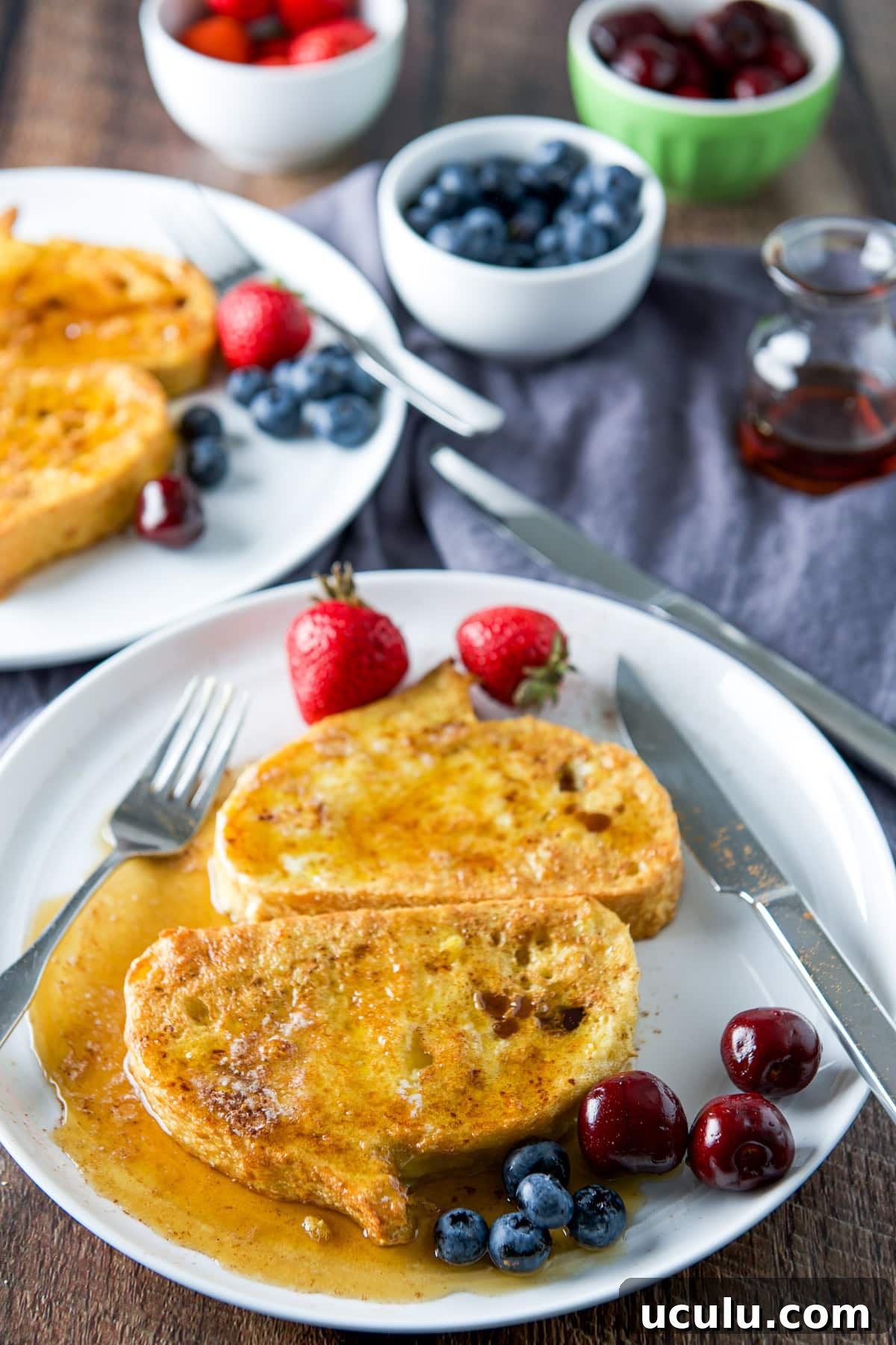 A high view of fruit on plates with French toast that has maple syrup on it