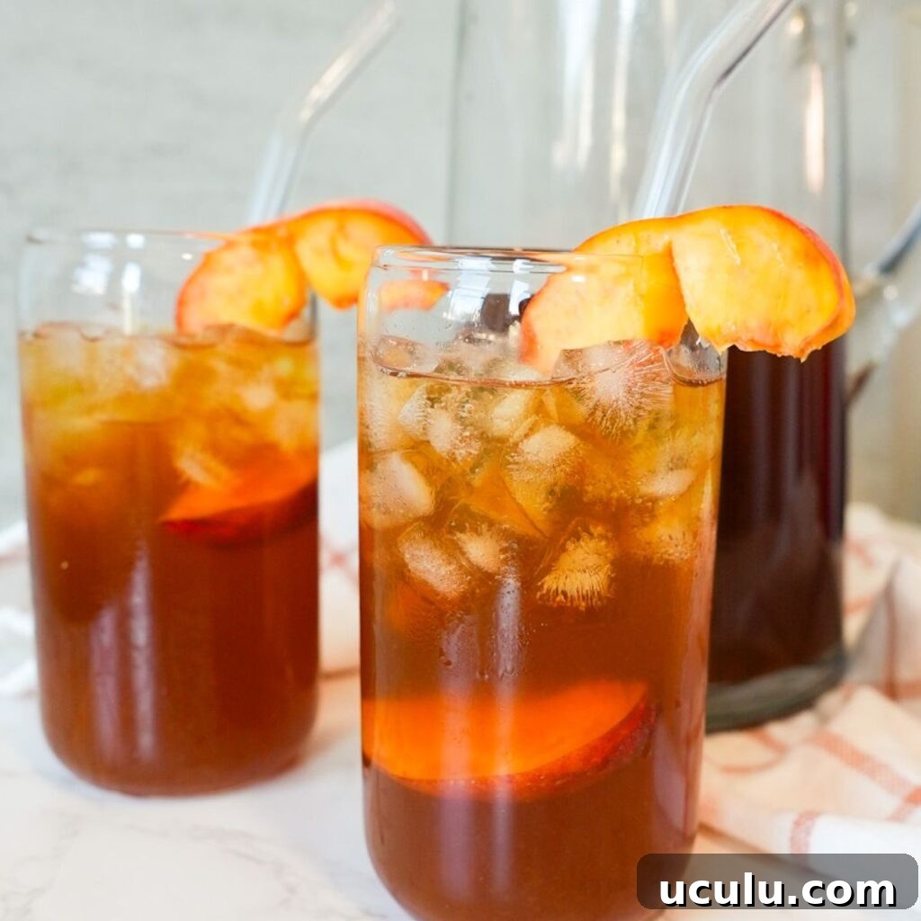 Two glasses of sweet peach tea with ice and fresh peach slices on top.