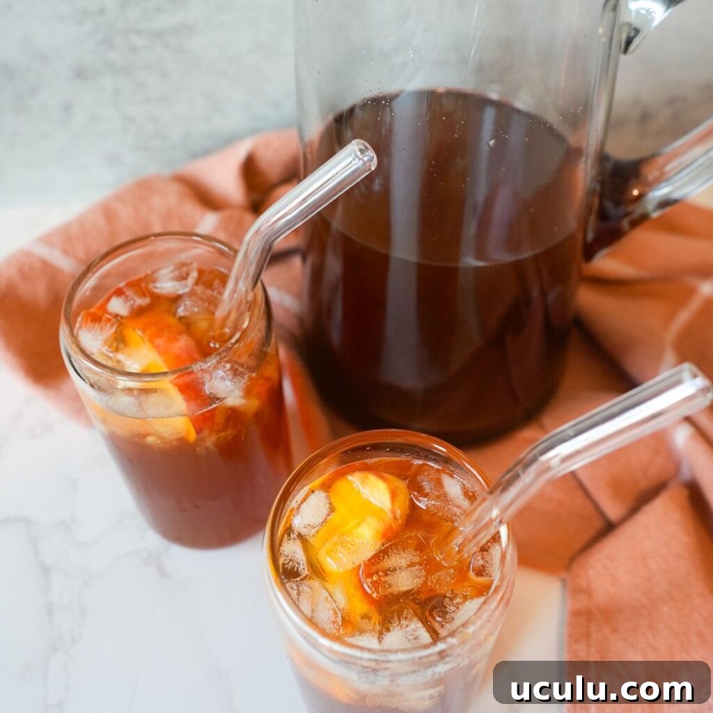 Peach sweet tea in a pitcher with two glasses of tea with ice.