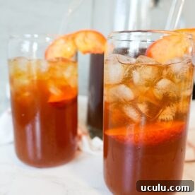 Two glasses of sweet peach tea with ice and fresh peach slices on top.