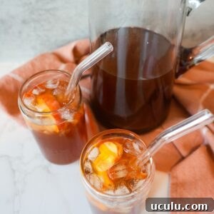 Peach sweet tea in a pitcher with two glasses of tea with ice.