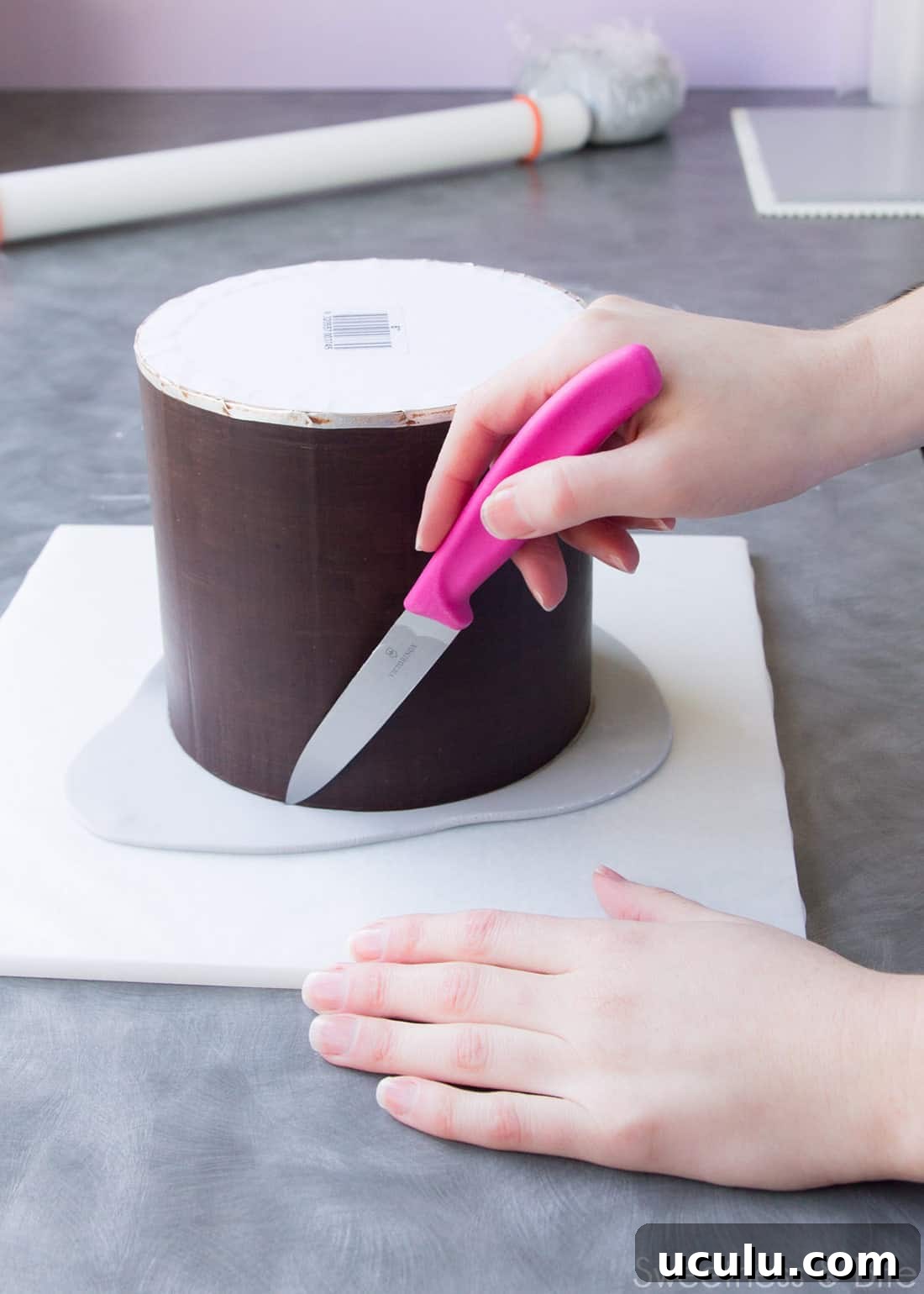 A hand using a small knife to trim the fondant on the upside down cake.