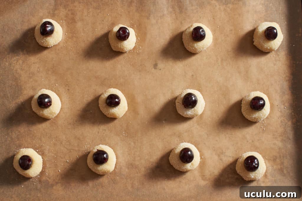 Amaretti cookie dough balls with cherries on parchment paper.