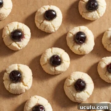 Amaretti cookies with a cherry on top of each one on brown parchment paper.