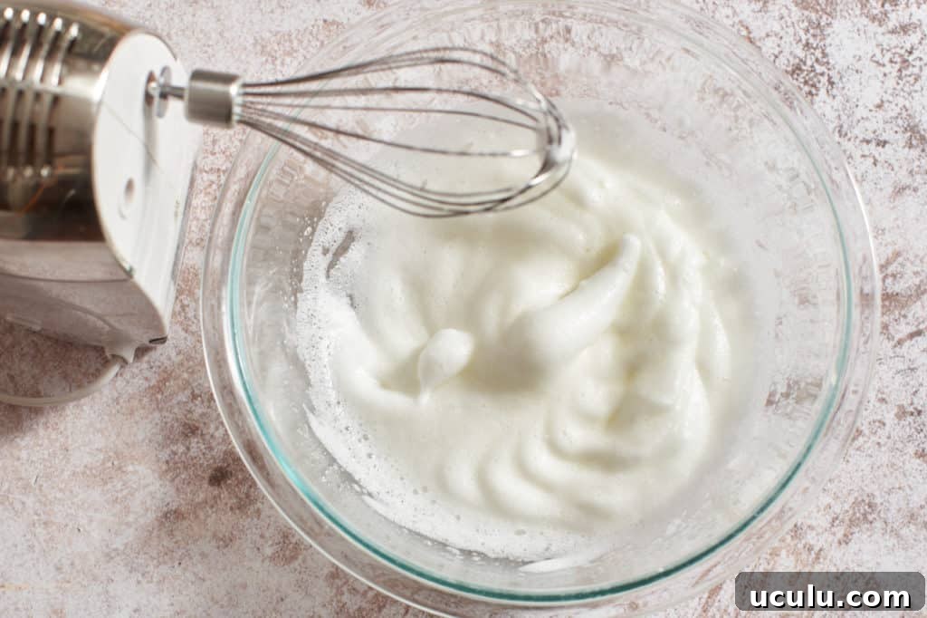 A hand mixer next to a bowl of whipped egg whites.