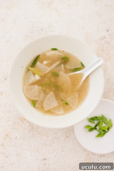 a bowl of mu guk next to a plate of freshly sliced green onions