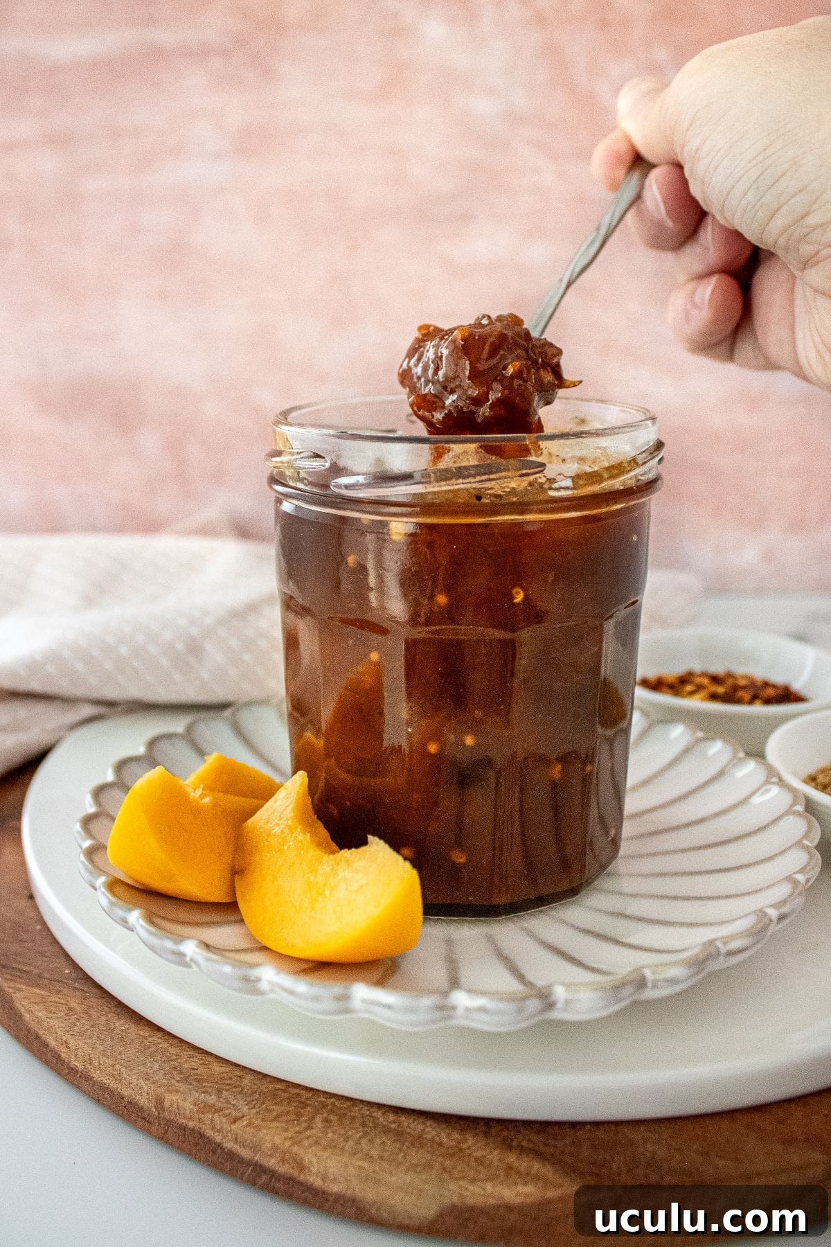 Open jar of Apricot Chutney on a small white plate, with a spoon scooping up some chutney.