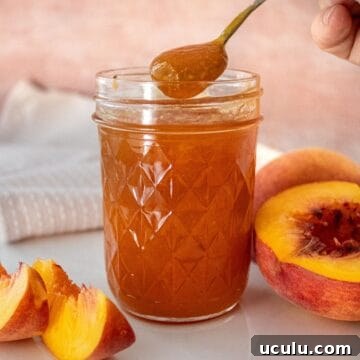 Open glass jar of Peach Jam sitting on a white plate, with a spoon scooping up some jam.