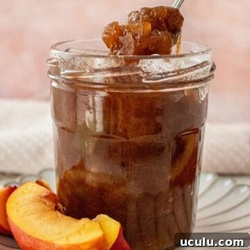Open glass jar of Nectarine Chutney, sitting on a small white plate, with a spoon scooping up some chutney.