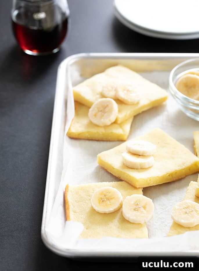 Gluten free pancakes made in a sheet pan, sliced on the baking tray, served with sliced bananas and maple syrup.