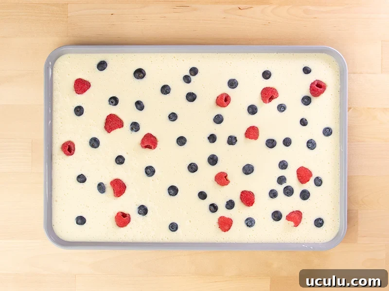 Raw sheet pan pancake batter with red and blue berries on top