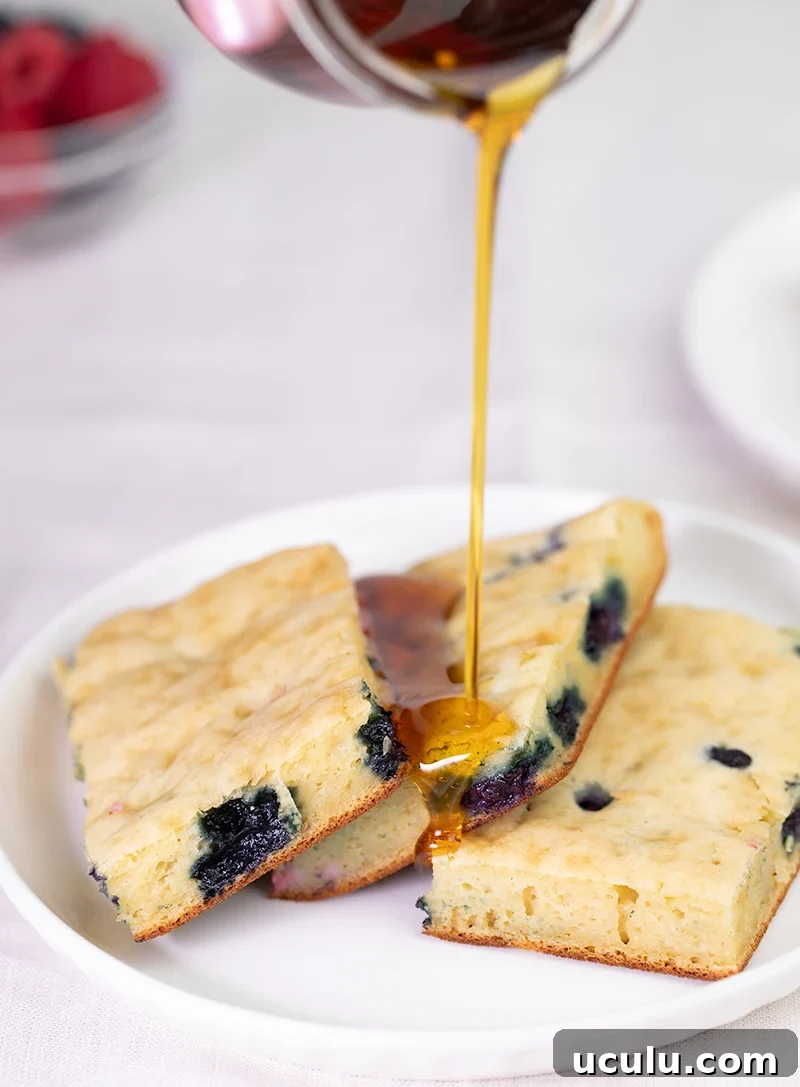 Syrup pouring onto white plate with 3 slices of sheet pan pancake