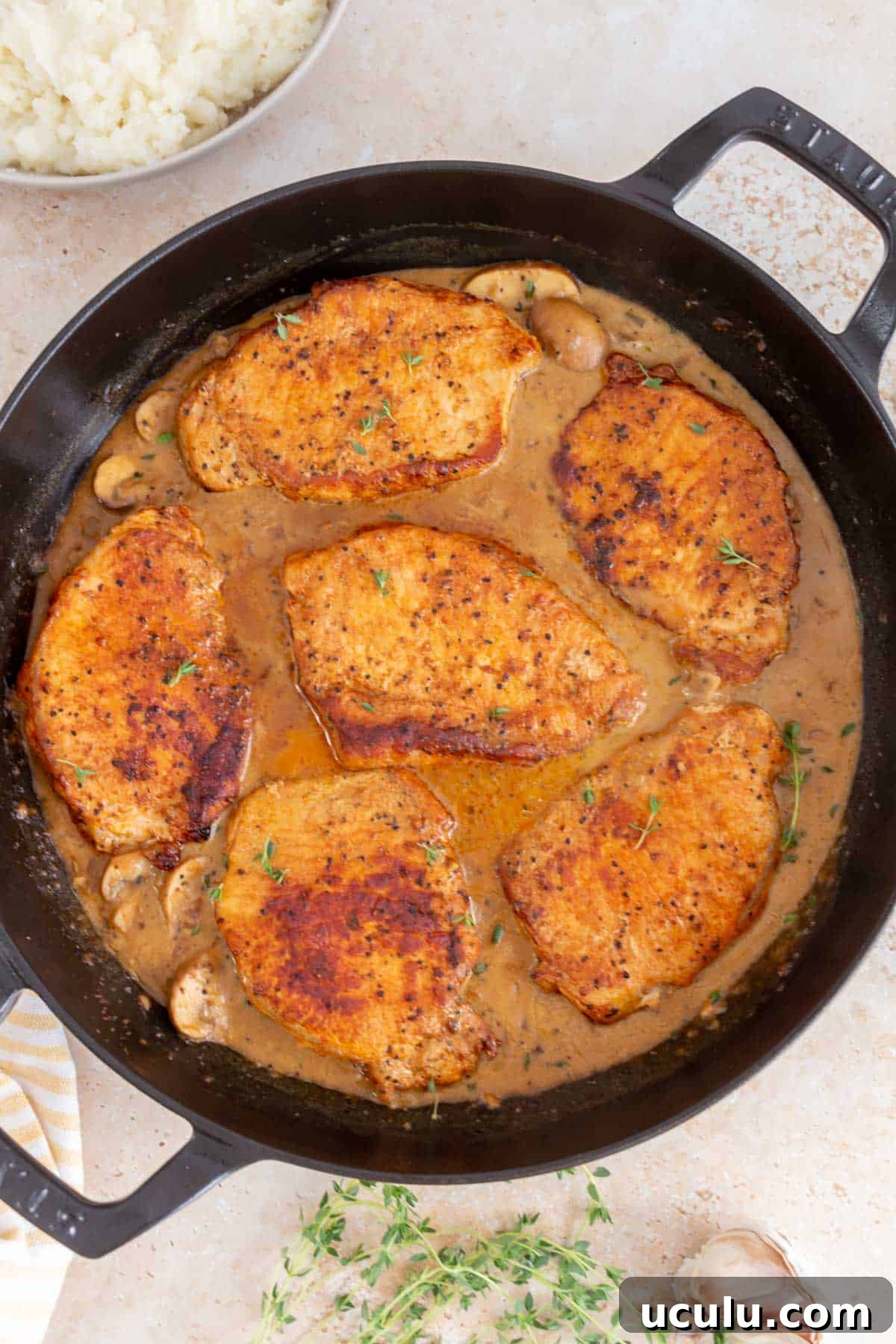Overhead view of dutch oven pork chops smothered in sauce. Garnished with fresh thyme.