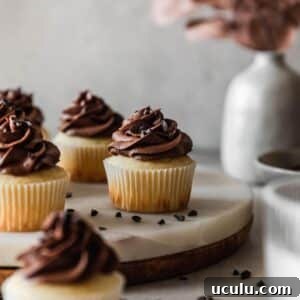 A very closeup image of high altitude yellow cupcakes with chocolate buttercream on a marble cake stand with a grey background.