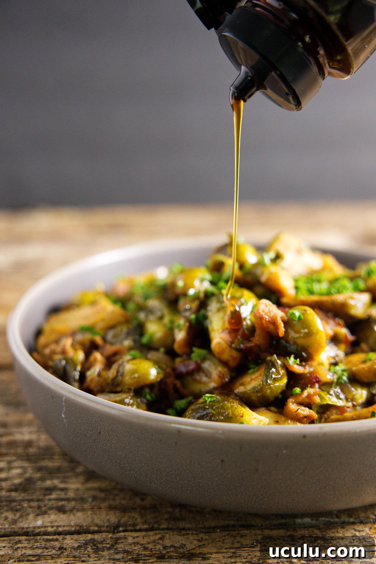 drizzle of honey falling on top of smoked brussels sprouts in a bowl