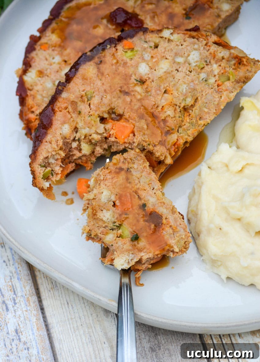a piece of cranberry turkey meatloaf with gravy on a silver fork resting on a white plate