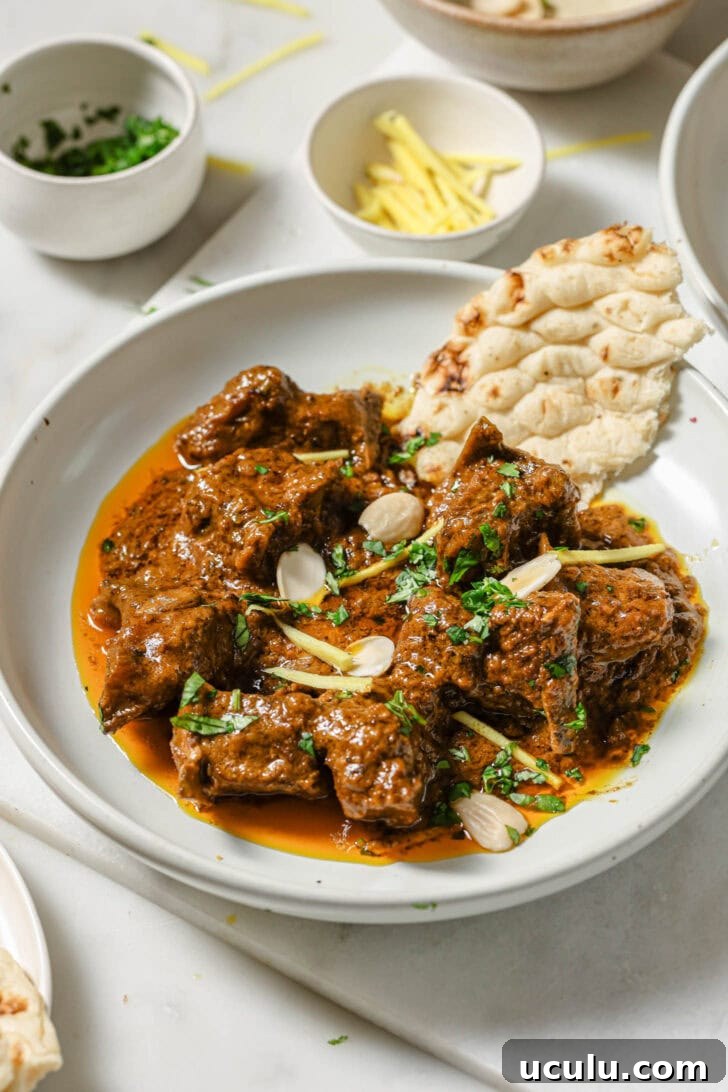 A plate of Mutton Korma garnished with almonds, julienned ginger and cilantro with a piece of naan on the side.
