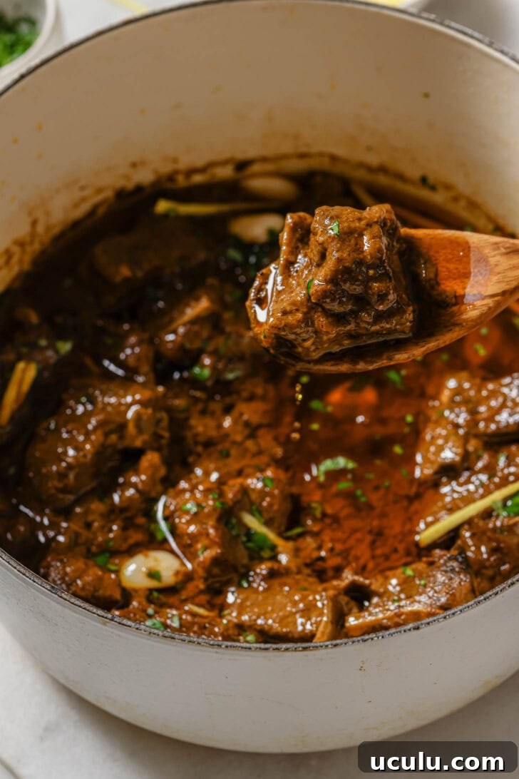 Holding a piece of saucy lamb over a pot of Lamb Korma.