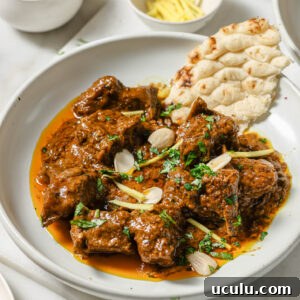 A plate of Mutton Korma garnished with almonds, julienned ginger and cilantro with a piece of naan on the side.