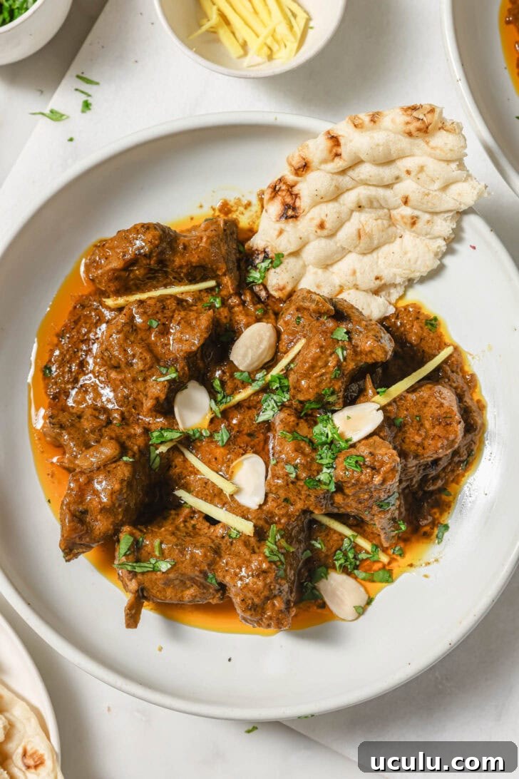 A plate of Mutton Korma garnished with almonds, julienned ginger and cilantro with a piece of naan on the side.