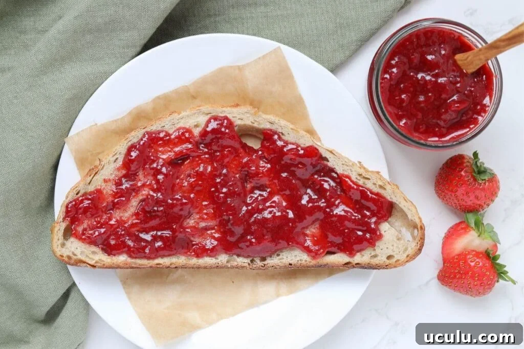 A slice of sourdough bread spread with strawberry jam sitting on a white plate.