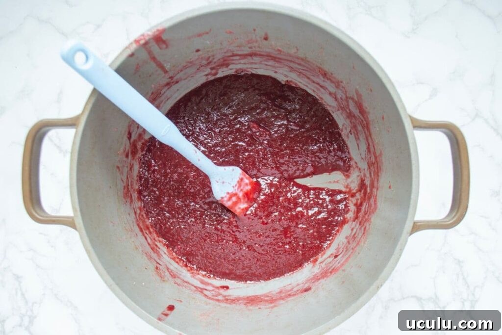 A large handled pot containing strawberry jam. The photo depicts the process of checking whether the jam is done by using a spatula in the base of the pan.