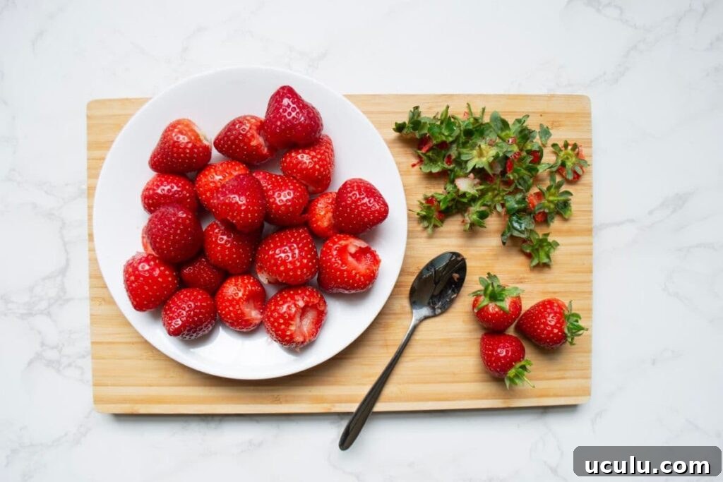 A wooden chopping board holding a whit plate with strawberries that have been hulled using a spoon.
