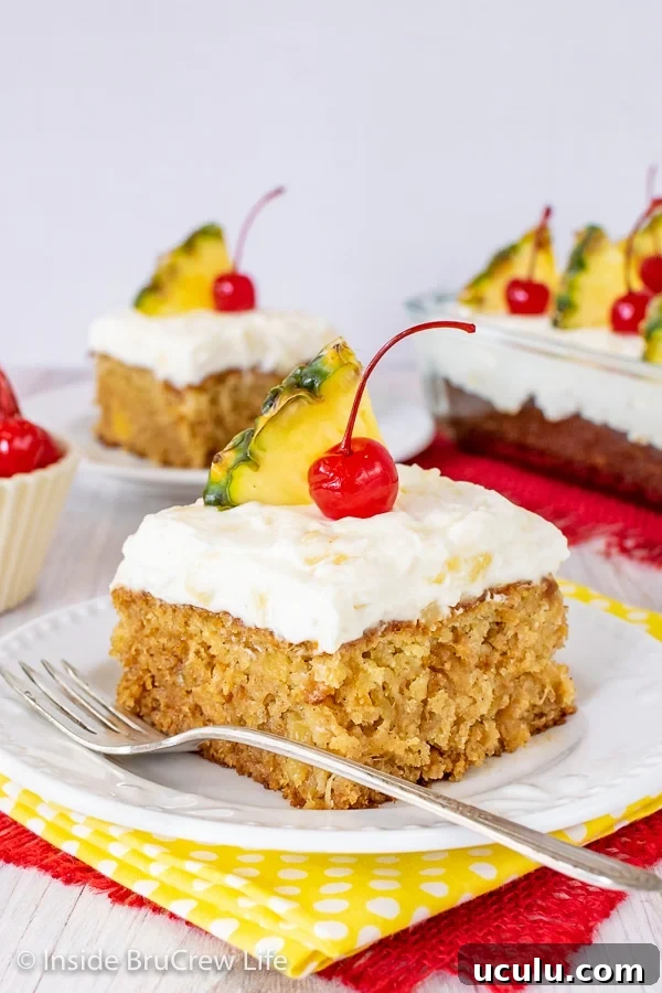 Two white plates with squares of pineapple sunshine cake topped with pineapple frosting and cherries on them