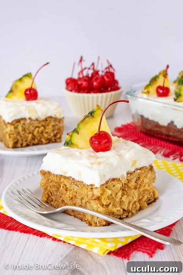 Two white plates with pineapple cake topped with pineapple cream cheese frosting, cherries, and pineapple slices.