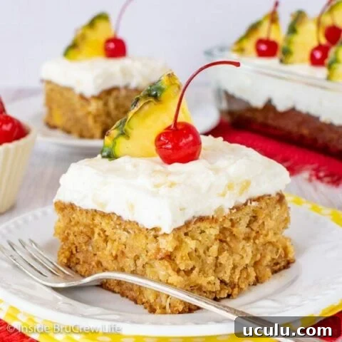 A white plate with a piece of pineapple cake topped with frosting, a cherry, and a pineapple wedge on it